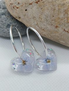 These exquisite handcrafted earrings feature real dried flowers, delicately preserved in clear resin. Each pair is truly one-of-a-kind, showcasing a unique blend of blue flowers and silver leaf, suspended on solid 925 sterling silver hoops. Details: Hoop Material: 925 Sterling Silver Hoop Size: 24mm Flower Setting: Clear Resin Please note that due to the natural variation of each flower, your earrings may differ slightly from the images shown, adding to their individual charm. For any additional Silver Pressed Flowers Drop Earrings, Silver Drop Earrings With Pressed Flowers, Silver Round Earrings With Pressed Flowers, Silver Sterling Flower Earrings With Pressed Flowers, Silver Pressed Flower Earrings In Resin, Silver Resin Earrings With Pressed Flowers, Silver Pressed Flower Resin Earrings, Silver Sterling Silver Earrings With Pressed Flowers, Sterling Silver Pressed Flower Drop Earrings