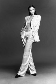 a woman in white pants and jacket posing for a black and white photo with her hands on her hips