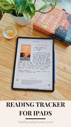 an ipad sitting on top of a wooden table next to a potted plant and a book