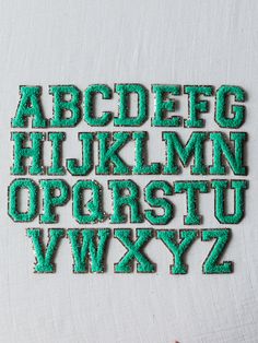 the upper and lower letters are made out of green glittery plastic beads, which have been sewn together