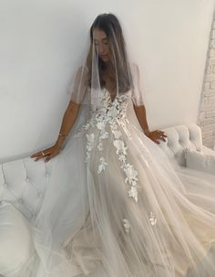 a woman in a wedding dress standing next to a white couch with her hands on the wall