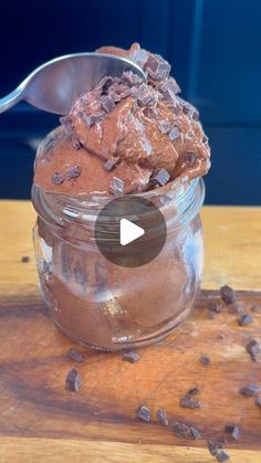 chocolate ice cream in a glass jar with a spoon sticking out of it on top of a wooden table