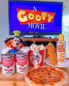 a pizza sitting on top of a wooden table next to cans of soda and a tv