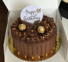 a birthday cake with chocolate frosting and gold stars on top, in a box