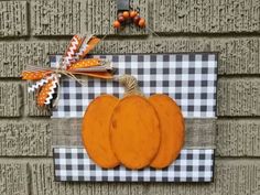 an orange pumpkin hanging on the side of a brick wall with a plaid ribbon around it