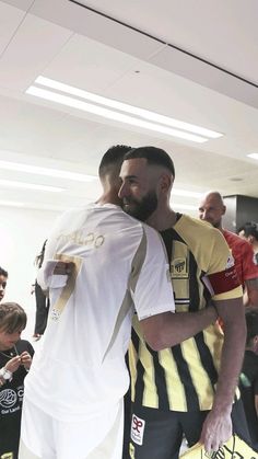 two men are hugging each other in the middle of a room full of people and one is wearing a yellow and white striped shirt