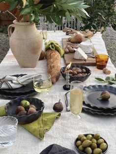 an outdoor table set with plates, bowls and glasses