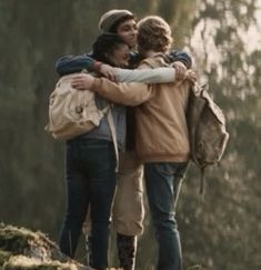 three people hugging each other on top of a hill