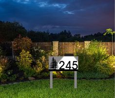 an illuminated sign in the middle of a garden at night with trees and bushes behind it