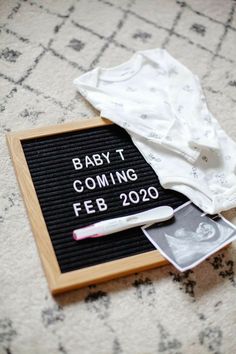 a baby t - shirt is laying on top of a black and white sign that says, baby t coming feb 20