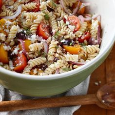 a bowl filled with pasta salad next to a wooden spoon