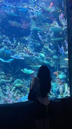 a woman standing in front of an aquarium looking at the fish and corals inside