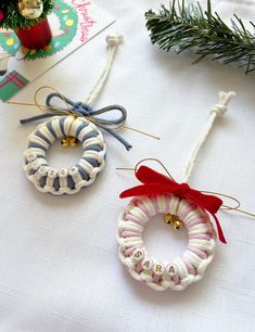 three christmas ornaments hanging from twine on a white tablecloth with pine branches and other holiday decorations