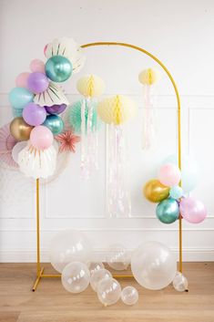 an arch with balloons and streamers hanging from it's sides in front of a white wall