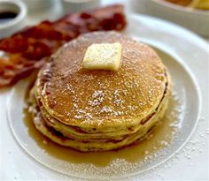 pancakes on a plate with butter and bacon in the background