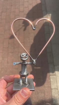 a person holding a small metal object in the shape of a heart with eyes and arms