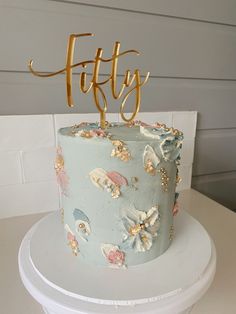 a blue cake with gold letters and flowers on it sitting on top of a white table