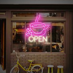 a neon sign that reads open with a cup of coffee on it and two bikes parked outside