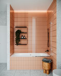 a bath tub sitting next to a white toilet under a bathroom window with pink tiles on the walls