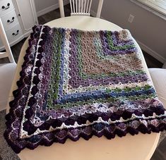 a crocheted blanket sitting on top of a wooden table next to a white chair