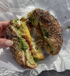 a person is holding up a sandwich with avocado and other toppings on it