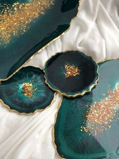 three green and gold plates sitting on top of a white cloth covered tablecloth with golden flecks