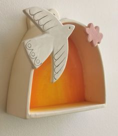 a white ceramic bird with a pink flower on it's tail hanging from the wall