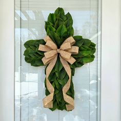 a cross made out of green leaves with a bow on the front door for decoration