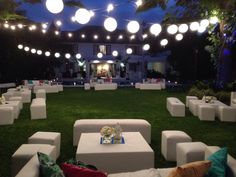 an outdoor seating area with white couches and lights strung over the lawn at night