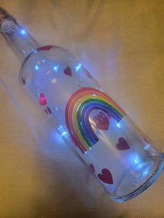 a glass bottle with hearts and rainbows on it sitting on a white cloth covered surface