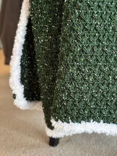 green and white knitted blanket with black metal legs on carpeted floor next to chair