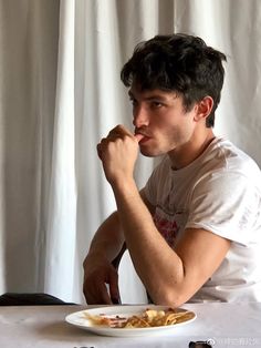 a young man sitting at a table with a plate of food in front of him