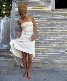 a woman in a white dress standing next to a building with her hands on her hips