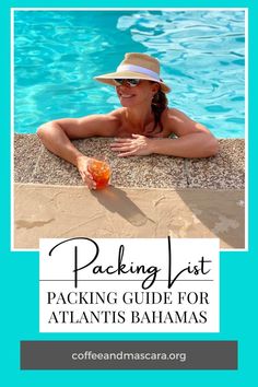 a woman in a hat and sunglasses sitting on the edge of a swimming pool holding an orange