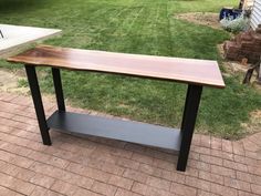 a wooden table sitting on top of a brick walkway next to a yard with grass