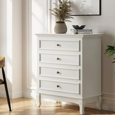 a white chest of drawers sitting next to a plant on top of a hard wood floor