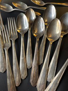 an assortment of antique silverware including spoons, forks and knives on a black surface