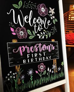 a chalkboard sign that says welcome to the person's first birthday with flowers on it