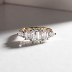 three stone diamond ring sitting on top of a white surface with sunlight coming through the window