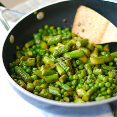 peas and asparagus in a pan with a wooden spoon