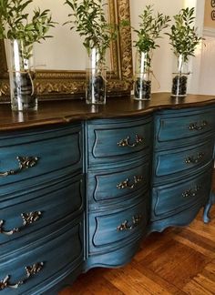 a blue dresser with plants in vases on top of it and a mirror behind it