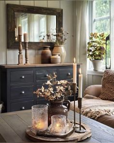 a table with candles and flowers on it in front of a couch, mirror and window