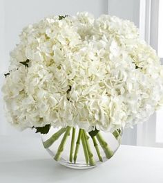 a vase filled with white flowers sitting on top of a table next to a window