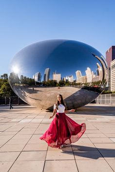 a woman standing in front of a large metal sculpture with her long red skirt blowing in the wind