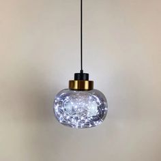 a clear glass light hanging from a black cord with white lights in the bottom and gold trim