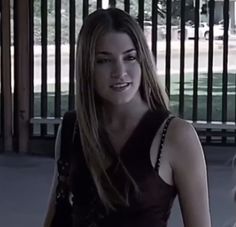 a woman standing in front of a fence with her hand on her hip and looking at the camera