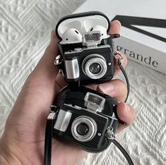 two black and white cameras sitting on top of a bed next to a box with ear buds