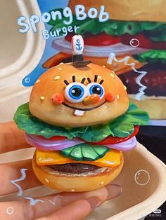 a hand holding a toy hamburger that looks like a burger with eyes and mouth painted on it