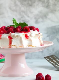 a white cake with raspberries and whipped cream on top is sitting on a pink pedestal