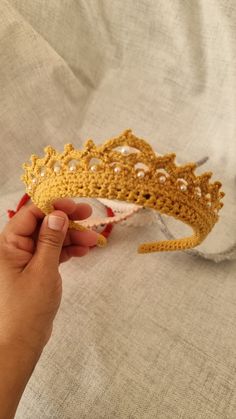 a hand holding a crocheted crown on top of a white cloth covered bed